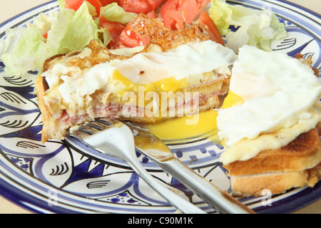 Ein Croque Madame - geröstetem Käse und Schinkensandwich garniert mit Bechamel-Sauce und Spiegelei - mit Tomaten und Salat-Salat Stockfoto