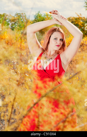 Schöne Auburn dunkelhaarige Frau draußen in der Natur, Herbst. Sie ist eine Kaukasische Frau trägt ein rotes Kleid. Stockfoto