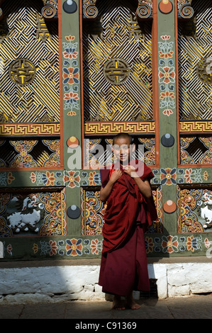 Ein junger Lehrling Mönch hält vor einem wunderschön geschnitzten und bemalten Fenster in Punakha Dzong, Bhutan. Stockfoto