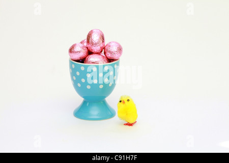 Ein kleines gefälschtes Huhn neben einem Eierbecher gefüllt mit Schokolade Ostereier Stockfoto