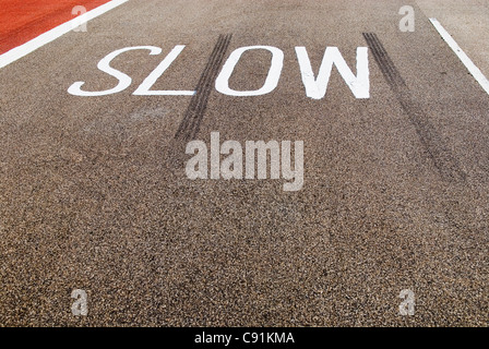 eine Warnung Schild mit der Aufschrift SLOW auf der Straße mit Bremsspuren daneben gemalt Stockfoto