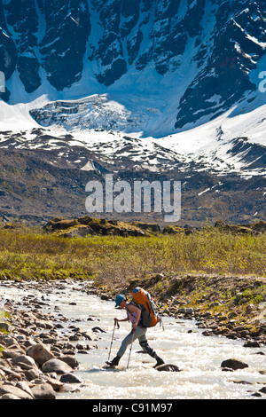 Weibliche Backpacker, die Überquerung des Babel-Flusses unter South Strebepfeiler an den westlichen Flanken des Gebirges Offenbarung, Alaska Stockfoto