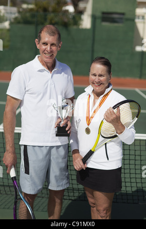 Älteres Ehepaar mit Trophäe auf Tennisplatz Stockfoto