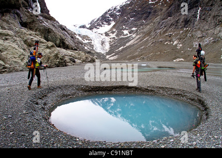 Männlichen Skifahrer Wandern mit Skiern um eine Moräne Wasserkocher Teich unterhalb des Eklutna-Gletschers, Chugach Mountains, Alaska, Frühling Stockfoto