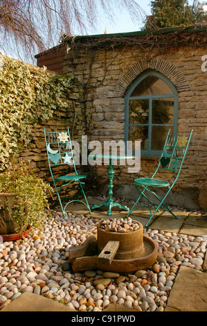 Metall-Stühle und Tisch mit Kies und Stein Terrasse mit Wasserspiel und Outdoor-Gartenhaus am englischen Garten. Stockfoto