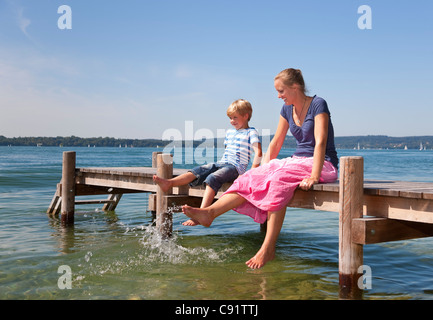 Mutter und Tochter, die Füße im See eintauchen Stockfoto