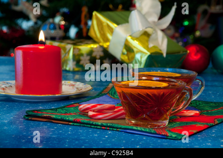 Nahaufnahme von heißen Apfelwein trinkt mit Orangenscheiben und eine brennende Kerze aus auf die Seite und verpackte Geschenke im Hintergrund Stockfoto