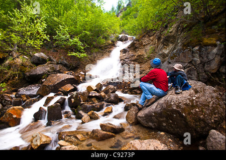 Vater und Sohn auf einer Wanderung ausruhen auf einem Felsen beim betrachten Cascade Falls Byers See im Denali Nationalpark, Alaska Stockfoto