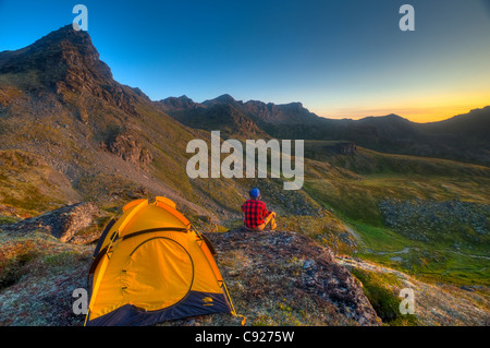 Ein Mann sitzt auf einem Felsen neben seinem Zelt beim camping in der Nähe von Hatcher Pass in den Talkeetna Bergen, Alaska Stockfoto