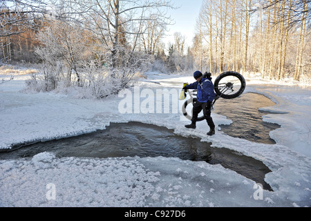 Radfahrer kreuzen Freiwasser Campell Creek während des Tragens ein Snowbike im fernen Norden Bicentennial Park in der Nähe von Anchorage, Alaska Stockfoto