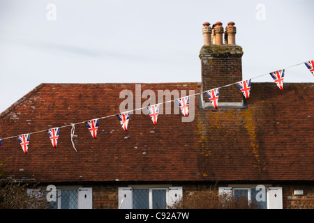Union Jack Girlanden Aufhängen in Pagham Dorf anlässlich die Pagham Kinderwagen Rennen, West Sussex, England Stockfoto