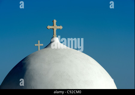 Blick auf Santorin Kirche Kuppel mit einem christlichen Kreuz und ein weiteres Kreuz im Hintergrund umrahmt von einem klaren blauen Himmel. Stockfoto