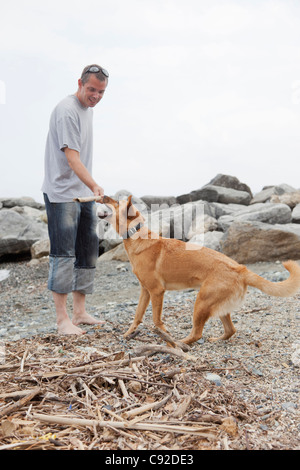 Mann mit Hund auf felsigen Strand spielen Stockfoto