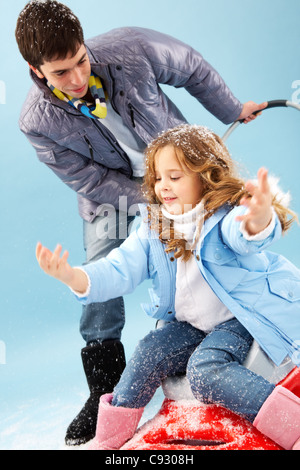 Glückliches Mädchen sitzen auf Schlitten und Schneeflocken mit ihrem Vater in der Nähe von Fang Stockfoto