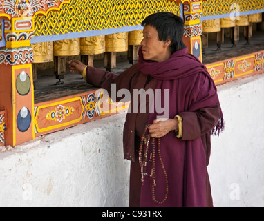 Eine Frau, Gebetskette in der Hand, dreht Messing Gebetsmühlen im 18. Jahrhundert Chorten Kora in Trashi Yangtze. Stockfoto