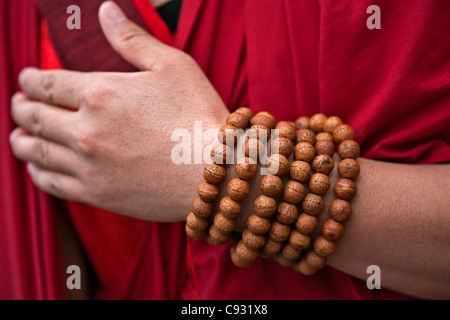 Gebetskette gewickelt runden das Handgelenk eines rot gekleideten Mönchs in der Nähe von Mongar. Stockfoto