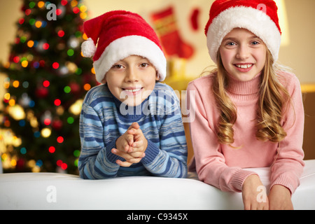 Entzückende Geschwister in Santa Hut lächelnd und Blick in die Kamera Stockfoto