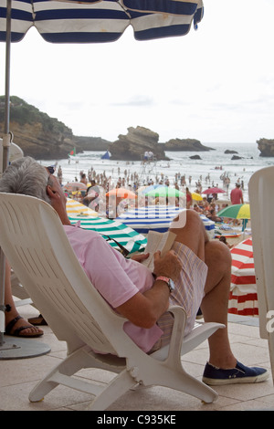 Älterer Mann entspannt im Liegestuhl mit einem Buch am Hauptstrand in Biarritz, Stockfoto