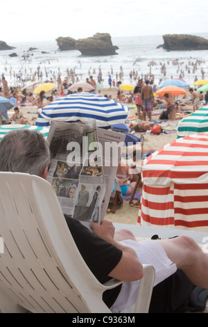 Älterer Mann entspannt im Liegestuhl mit einer Zeitung am Hauptstrand in Biarritz, Frankreich Stockfoto