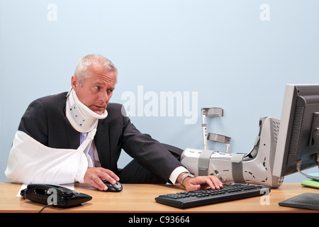 Foto eines ausgereiften Geschäftsmann mit multiplen Verletzungen sitzt an seinem Schreibtisch, die kämpfen, um an seinem Computer arbeiten. Stockfoto