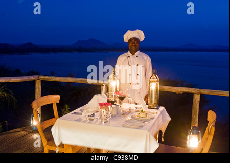 Malawi, Lake Malawi National Park.  Ein Koch steht vom Tisch auf der Veranda eines Chalets. Stockfoto