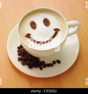 Cappuccino Kaffee mit einem Schokoladenpulver Smiley auf der Oberseite und Kaffeebohnen auf der Untertasse. Stockfoto