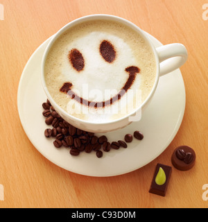 Cappuccino Kaffee mit Schokoladenpulver Smiley Gesicht an der Spitze mit Kaffeebohnen und Pralinen. Stockfoto