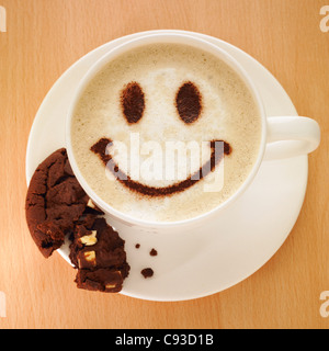 Cappuccino Kaffee mit Smiley-Gesicht in Kakaopulver und ein Cookie auf der Untertasse. Stockfoto