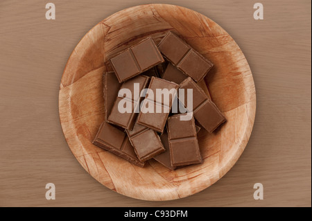 Köstliche Milchschokoladenstücke in einer Holzschale, die von oben auf einer dunklen Holzoberfläche fotografiert wurde Stockfoto
