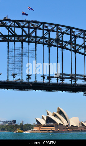 Blick auf das Wasser von der Fähre auf das Opernhaus von Sydney, eine Fährüberfahrt vor dem Hotel und Touristen, die hoch über die Sydney Harbour Bridge in Australien laufen Stockfoto