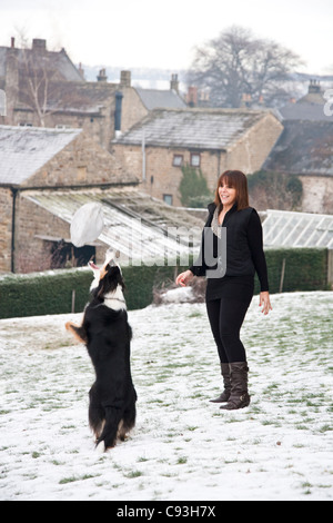 Eine Frau mit ihrem Border-Collie-Schäferhund im Schnee Stockfoto