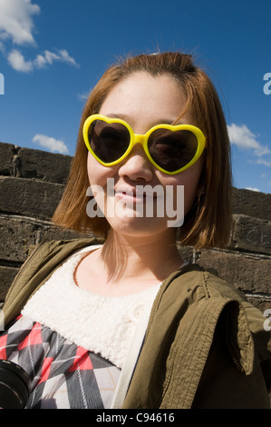 Ein chinesisches Mädchen mit gelben herzförmige Sonnenbrille auf der chinesischen Mauer bei Mutianyu nahe Beijing China Stockfoto