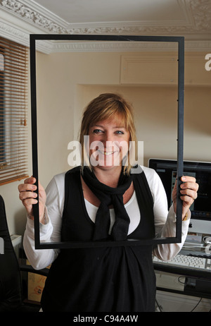 Frau arbeitet im Büro durch leeren Grafikrahmen lächelnd fotografiert November 2011 Stockfoto