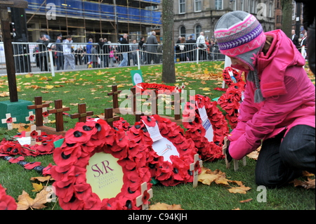 Ein junges Mädchen Pflanzen ein Kreuz mit einem Mohn in Glasgows Garden of Remembrance während Tag des Waffenstillstands gedenken. Stockfoto