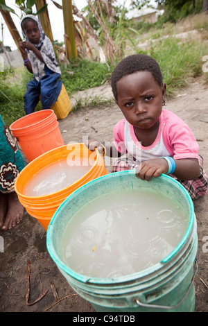 Ein Kind sitzt mit schmutzigem Wasser an einem Brunnen außerhalb Dar Es Salaam, Tansania, Ostafrika. Stockfoto