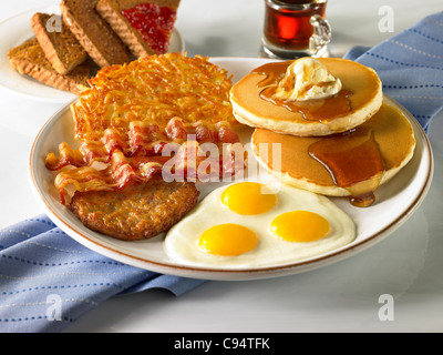 Ein Power-Frühstück mit drei Eiern, Wurst, Speck, Rösti, Pfannkuchen mit Sirup, Butter und toast Stockfoto