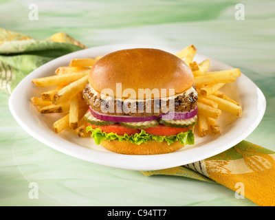 Hamburger auf einem Brötchen mit Salat, Tomaten, Gurken und Zwiebeln serviert mit Pommes frites Stockfoto