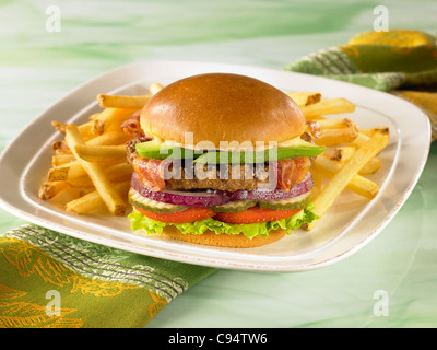 Ein Avocado Bacon Burger auf einem Brötchen mit Salat, Tomate, Gurke und Zwiebel serviert mit Pommes frites Stockfoto
