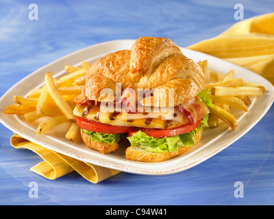 Gourmet-Croissant-Hähnchen-Sandwich mit Speck, Salat, Tomaten und Käse, serviert mit Pommes frites Stockfoto