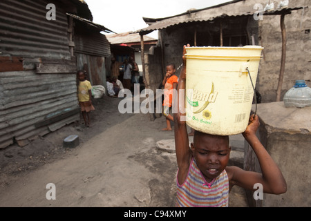 Ein junges Mädchen hebt einen Eimer mit Wasser auf den Kopf in Dar Es Salaam, Tansania, Ostafrika. Stockfoto