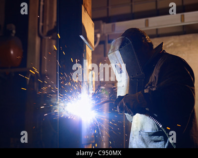 Arbeiter im Stahlwerk mit Schweißen Maske, Werkzeuge und Maschinen auf Metall. Horizontale Form, Seitenansicht, Hüfte aufwärts Stockfoto