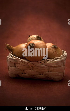 ein Korb mit Zwiebeln gegen einen dunkelroten Hintergrund Stockfoto