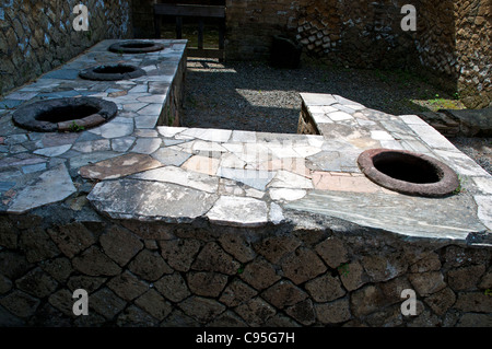 Ein Thermopolium mit großen Tonkrügen (Dolia) eingebettet in einem unverwechselbaren gefliesten Mauerwerk-Zähler in der Front, Herculaneum Stockfoto