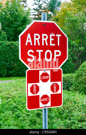 Zweisprachige 4-Wege Stop-Schild umgeben von viel Grün. Aufgenommen in der Provinz Quebec, Kanada. Stockfoto