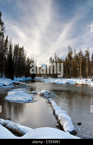 Winterschnee bedeckten Ufer eines kleinen Flusses Wind durch einen Wald von Bäumen Stockfoto