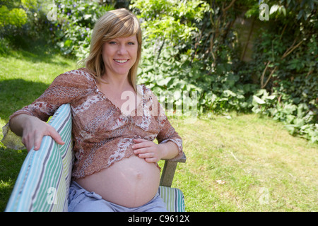 Schwangere Frau sitzen auf einer Gartenbank. Sie ist 35 Wochen schwanger. Stockfoto