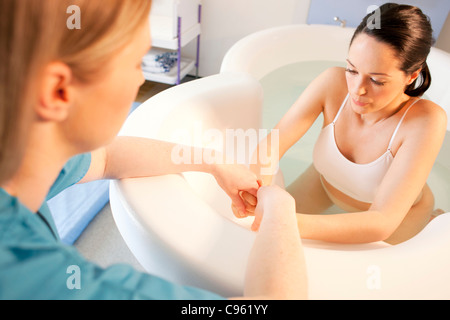 Wassergeburt. Hand in Hand einer schwangeren Frau, die in einem Geburt Pool ist Hebamme. Stockfoto