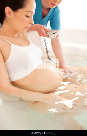 Wassergeburt. Hebamme mit einem doppler Monitor Herzschlag eines Fötus in einem Geburt Pool anhören. Stockfoto