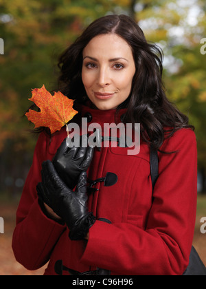 Porträt einer schönen Frau, die ein rotes Ahornblatt in ihren Händen hält Stockfoto