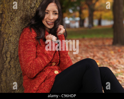 Wunderschöne lächelnde Frau in einem roten Pullover kuscheln. Deckung aus Wind in Herbstwetter. Stockfoto